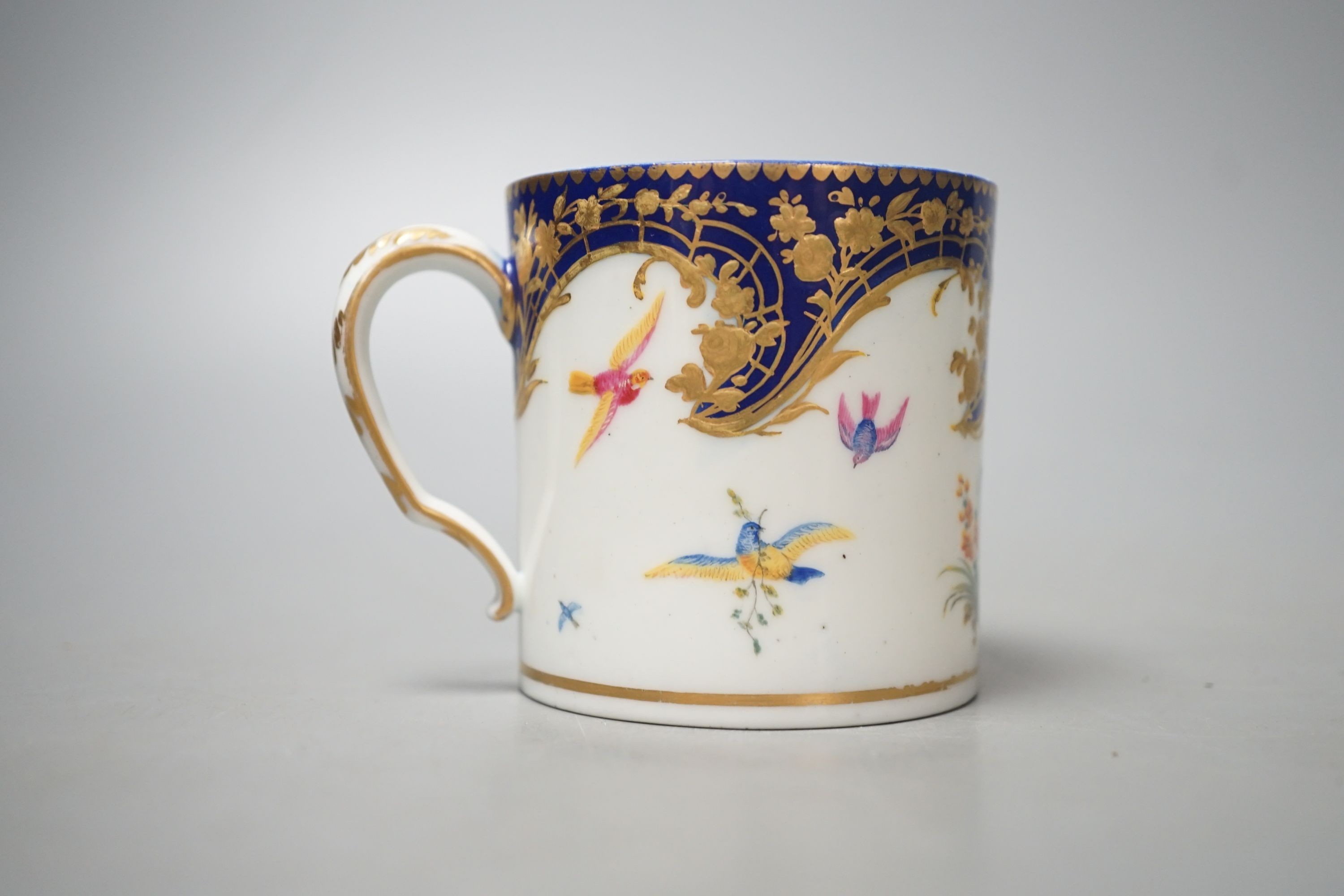 A Sevres coffee can painted with two birds in a tree, and other birds in flight under a richly gilded blue ground date code for 1766